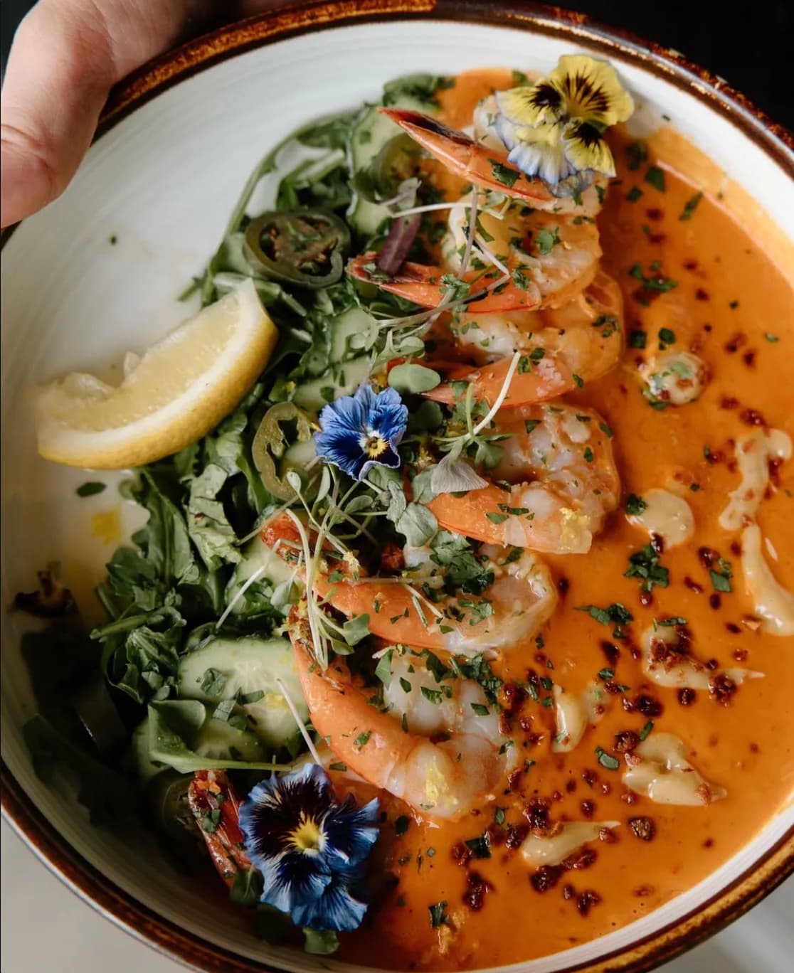 The original photo: shrimp in a bisque-style sauce with herbs and edible flowers, in a white bowl.